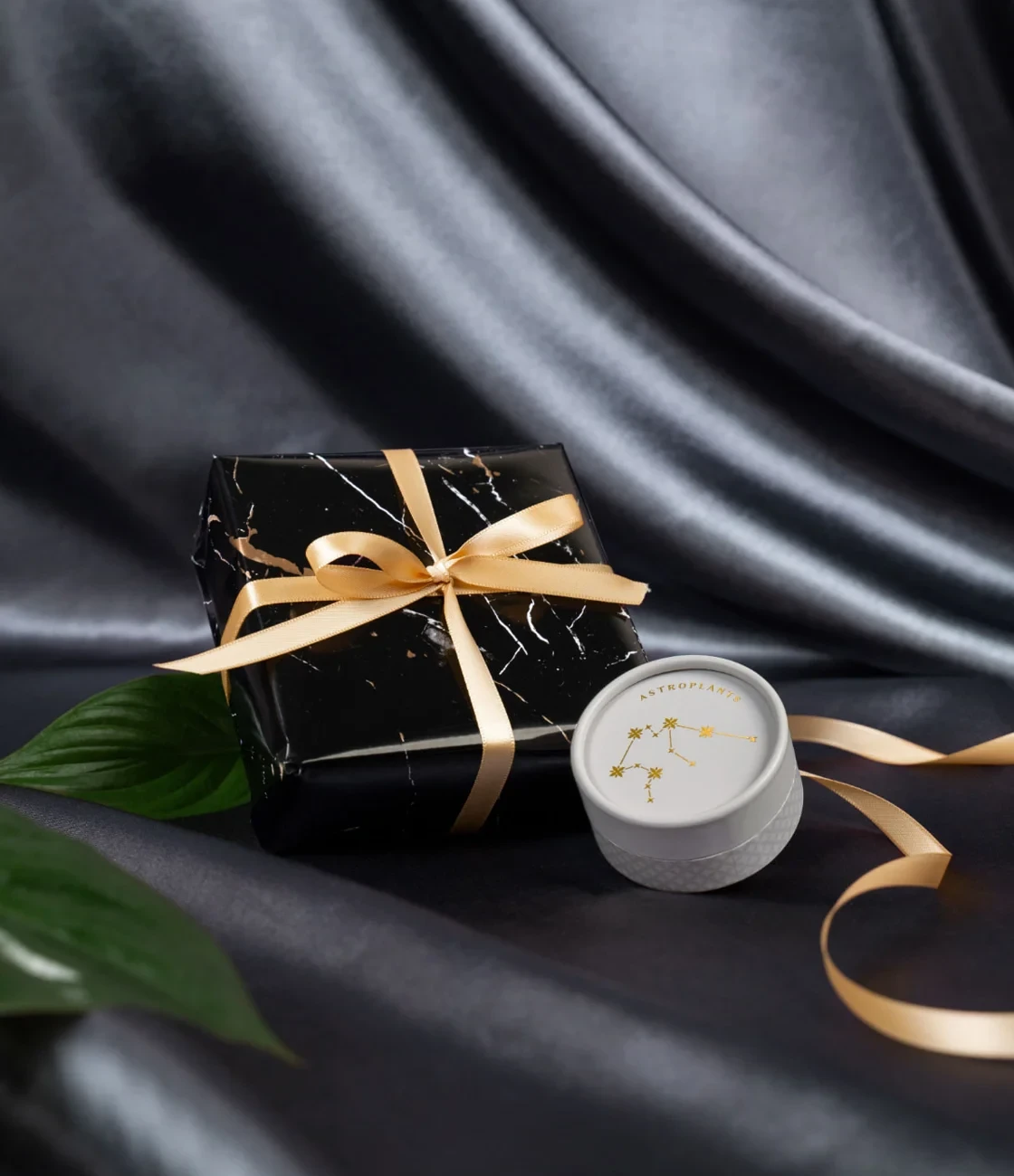 Dose neben schwarz-marmoriertem Geschenkpäckchen mit goldenem Band auf dunkler Seide