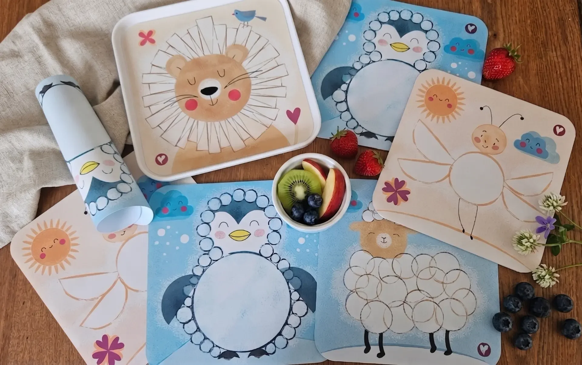 Vier Kinderteller mit Löwe, Pinguin, Schaf und Biene, umgeben von Obst auf einem Holztisch